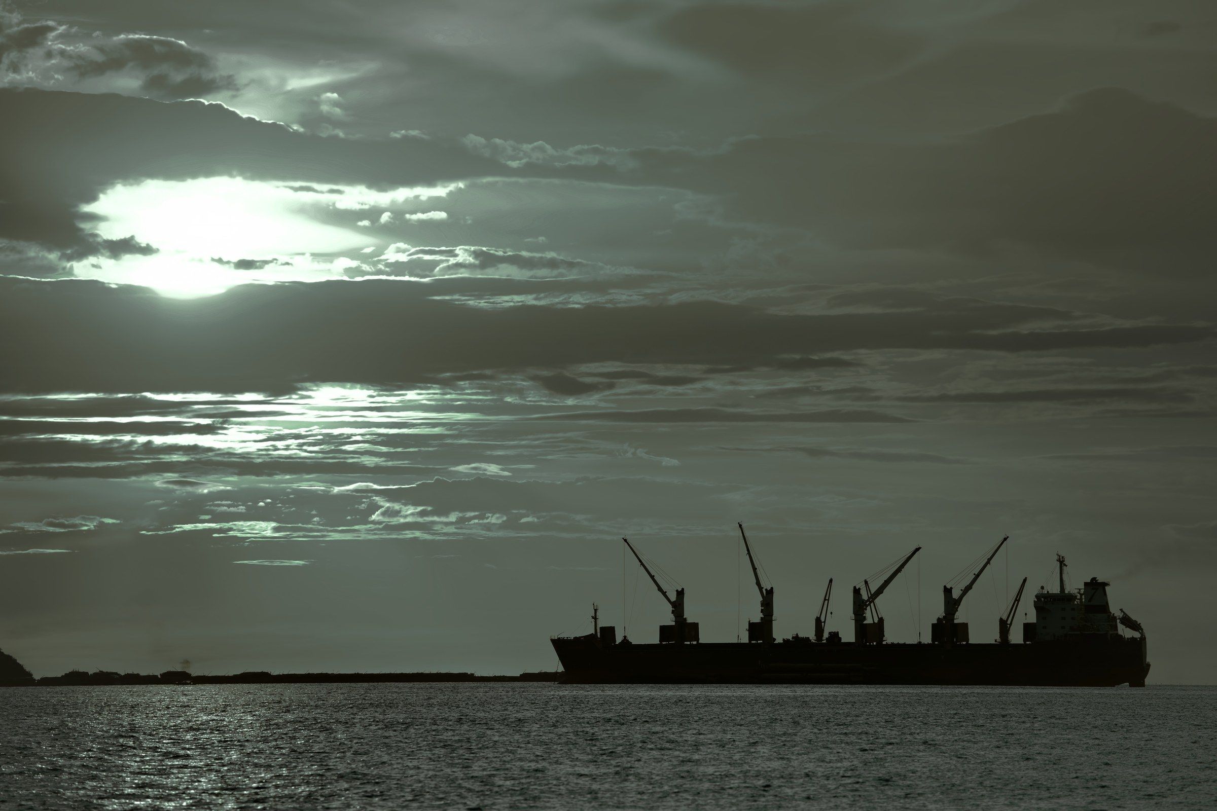 A cargo ship and harbour cranes in silhouette at dusk.